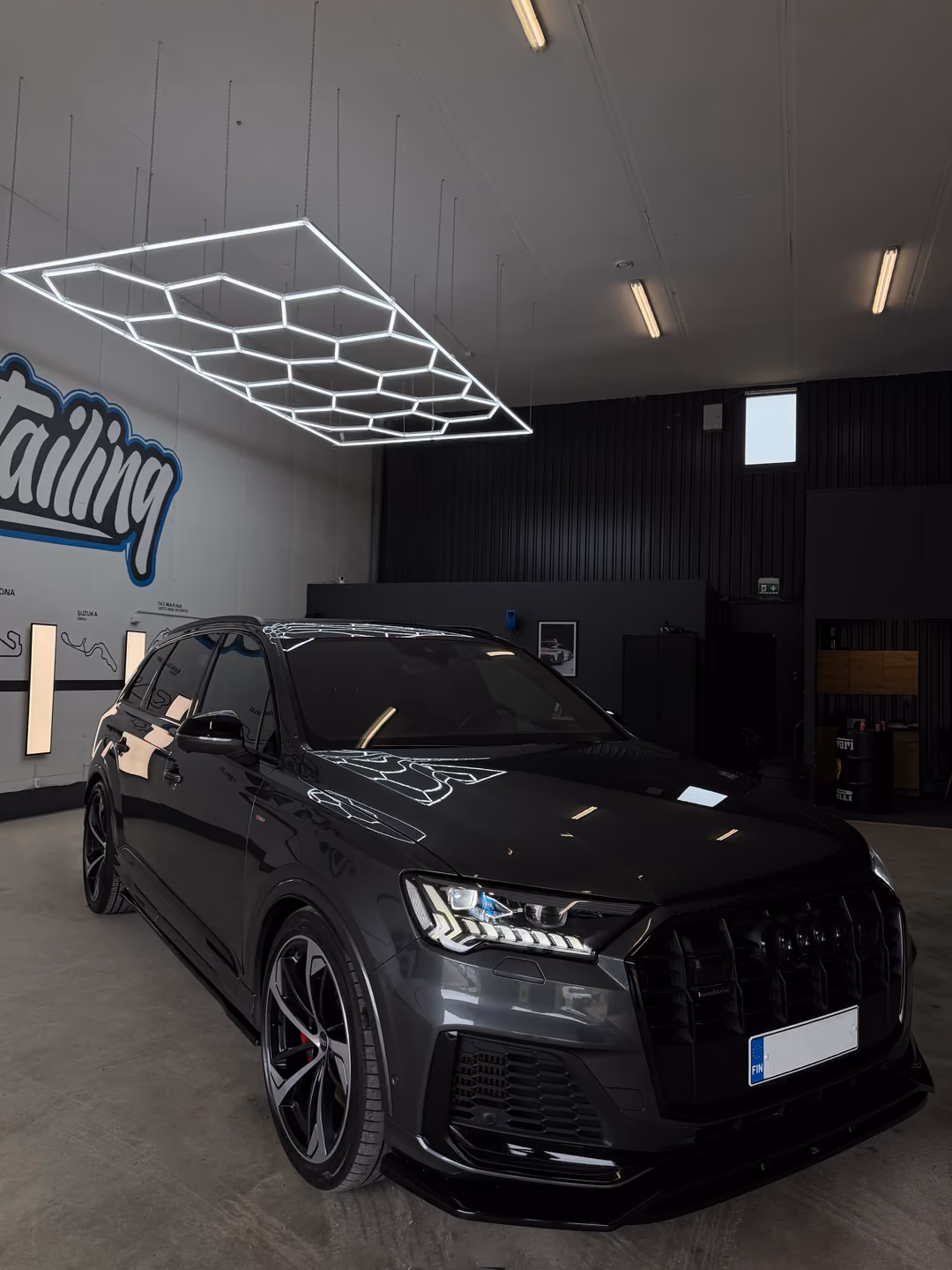 Kiillotettu harmaa Audi Q7 KM-Detailingin hallissa: kuusikulmiovalot heijastuvat konepellistä ja tuulilasista