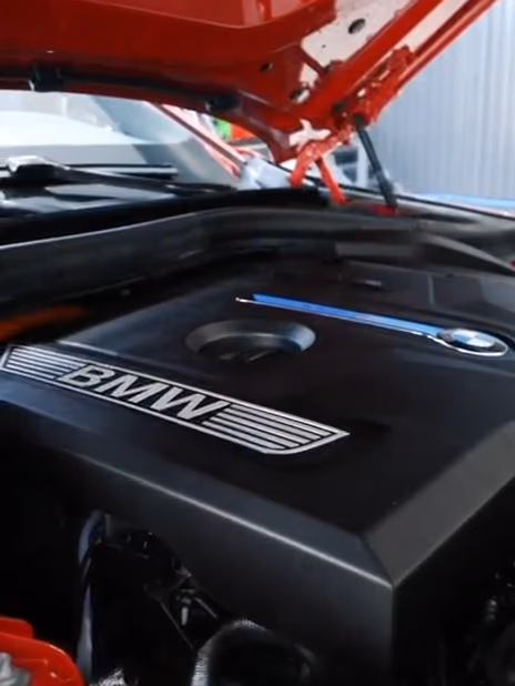 Punaisen BMW:n moottoritila konepelti auki: moottorin suojakansi ja BMW-logo