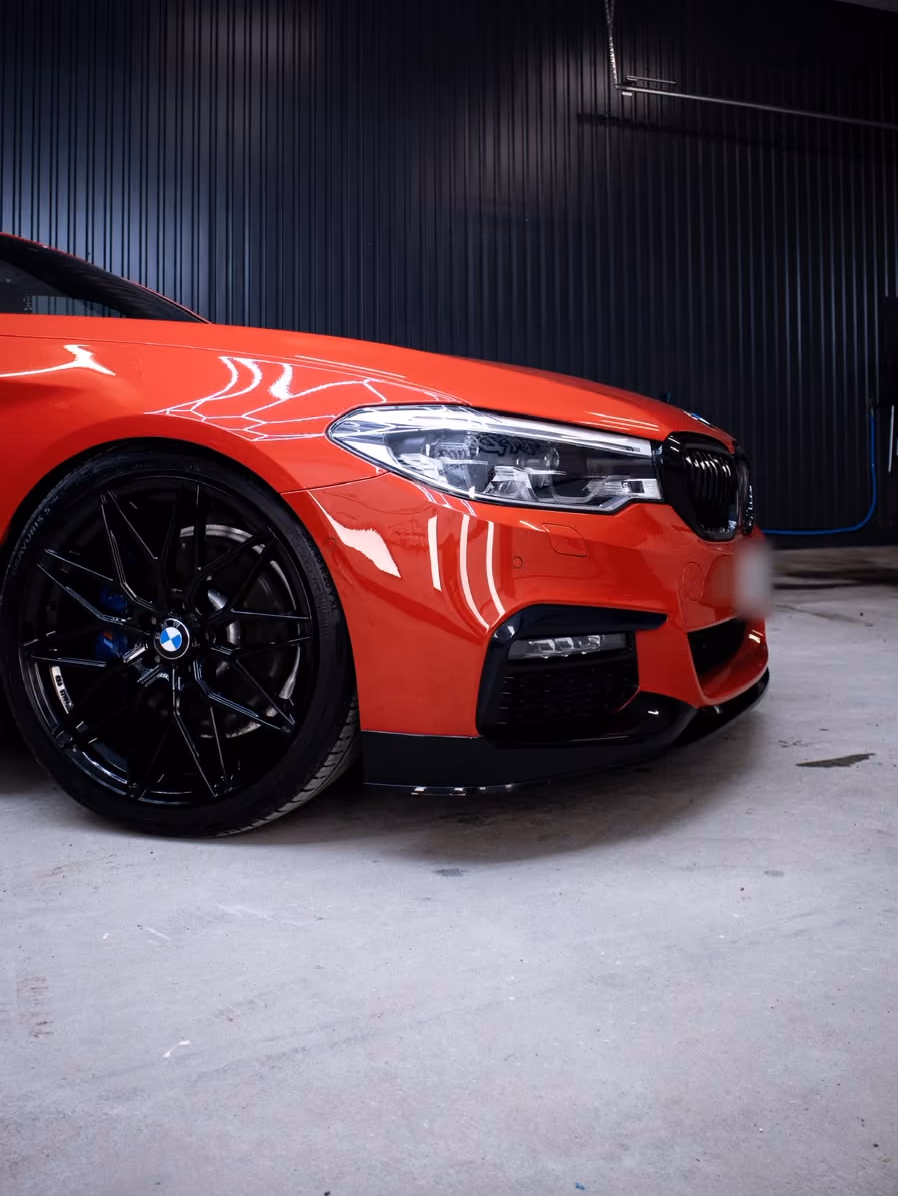 Punaisen BMW:n keula, ajovalo ja musta vanne kiiltävinä hallissa